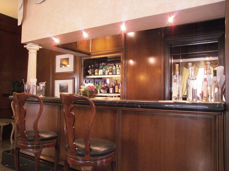 Bar mit dunklem Holz, elegantem Tresen und drei hohen Stühlen in warm beleuchtetem Raum.