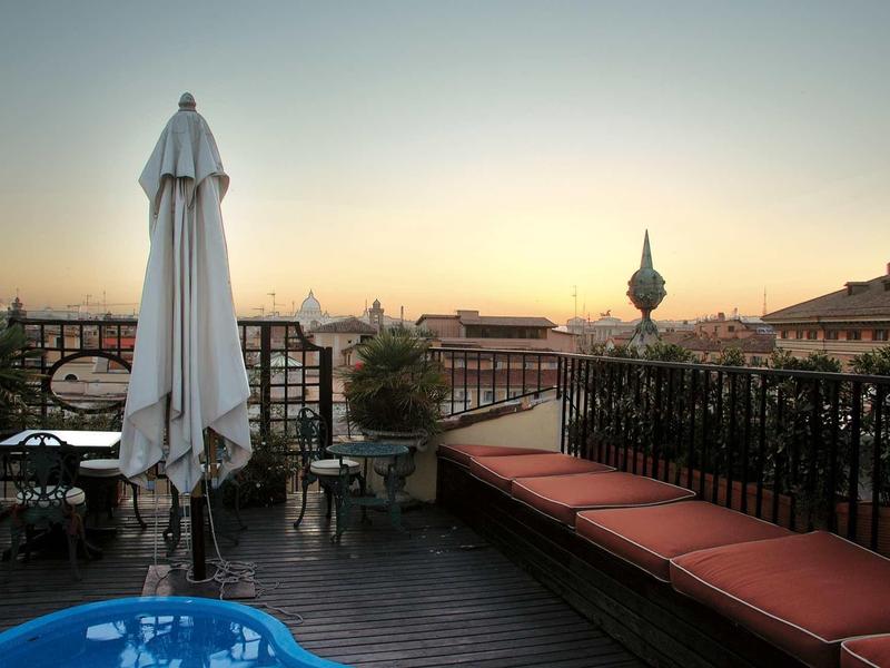 Dachterrasse mit Sitzbank, Tisch, Stühlen, geschlossenem Sonnenschirm und kleinem Pool bei Sonnenuntergang.