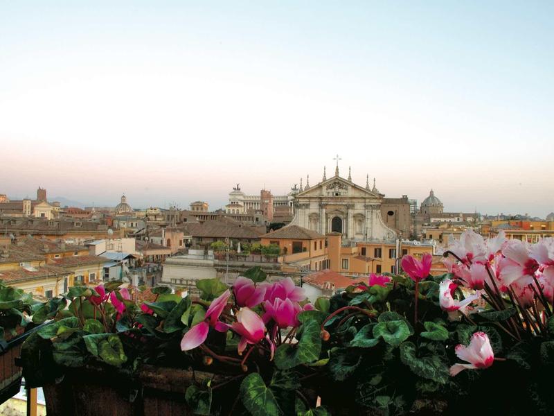 Stadtpanorama bei Sonnenaufgang mit Kirche im Hintergrund und pinken Blumen im Vordergrund.