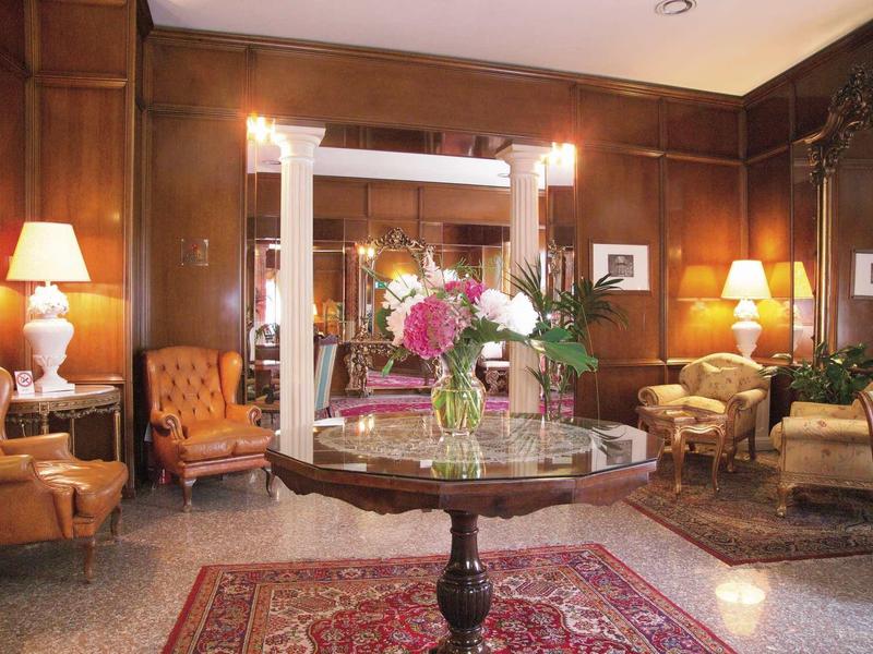 Elegantes Wohnzimmer mit Holzvertäfelung, Teppich, Blumen auf Marmor-Tisch und warmem Lampenlicht.