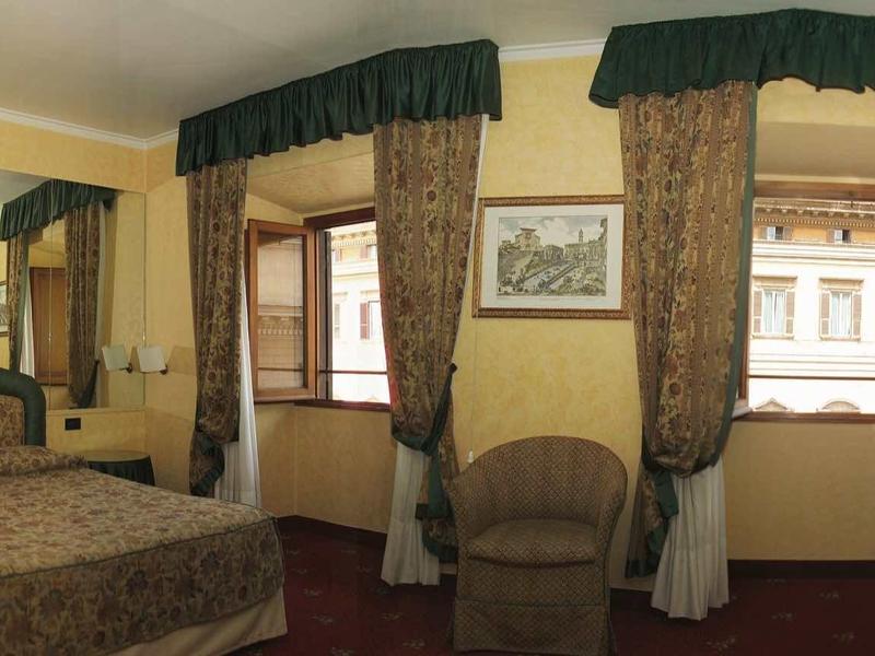 Gemütliches Schlafzimmer mit Doppelbett, Sesseln, großen Fenstern und braun-grünen Vorhängen.