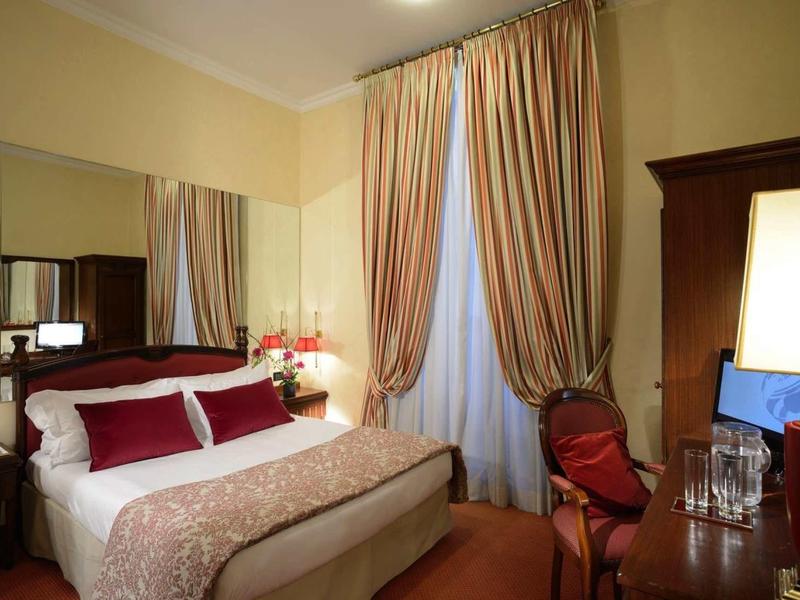 Elegantes Schlafzimmer mit großem Bett, Spiegelwand, roten Kissen und langen Vorhängen.