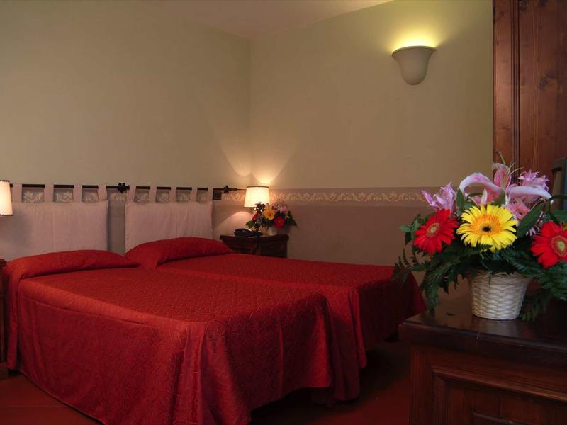 Gemütliches Schlafzimmer mit roten Bettüberwürfen, Nachttischen und bunter Blumenarrangement.