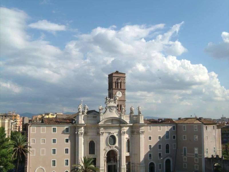 Große barocke Kirche mit hohem Turm, Palmen im Vordergrund und blauem Himmel mit Wolken.