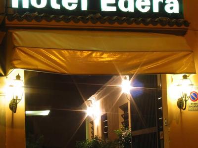 Leuchtendes Schild "Hotel Edera" über dem Eingang eines Gebäudes bei Nacht.