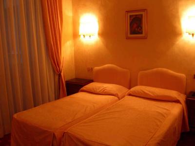 Two single beds with orange covers in a warmly lit hotel room.