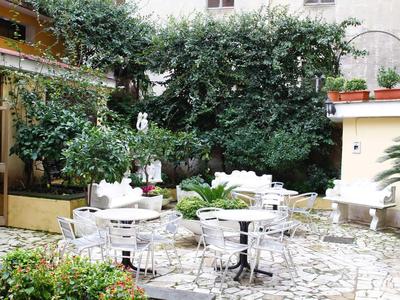 Cozy hotel outdoor area with white tables, chairs, and lush greenery.