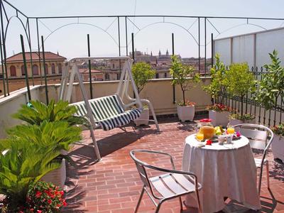 Cozy rooftop terrace with seating, plants, and city view under clear sky.
