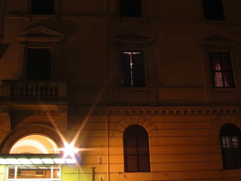 Illuminated hotel entrance with plants in front of a multi-story building at night.
