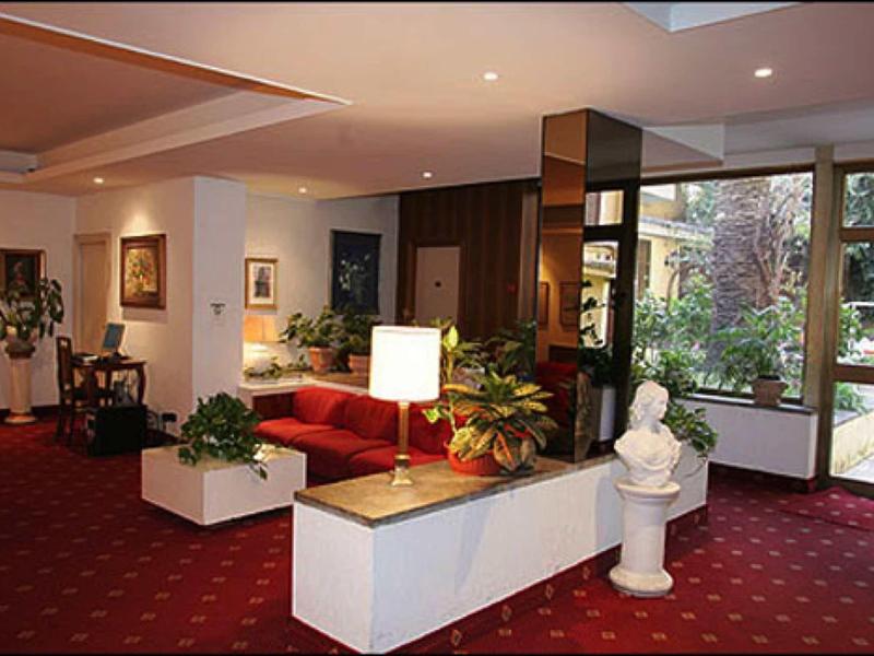 Hotel lobby with red carpet, seating area, plants, and sculpture near large windows.