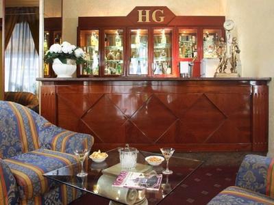 Elegant bar with wooden paneling, glass display case, and patterned armchairs in warm tones.