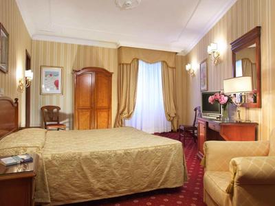 Elegant hotel room with double bed, wooden furniture, and red carpet flooring.