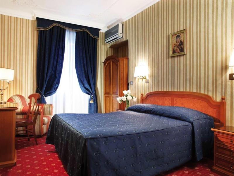 Cozy hotel room with double bed, dark blue curtains, and striped wallpaper.