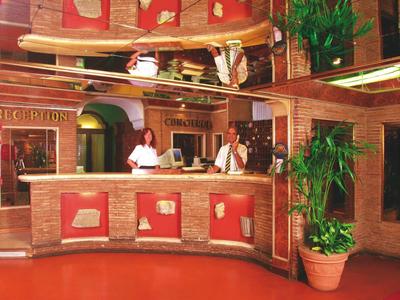 Hotel reception with two staff, rustic wooden design and indoor plants.
