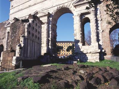 Ancient stone gate with arches against clear blue sky and some grass in the foreground