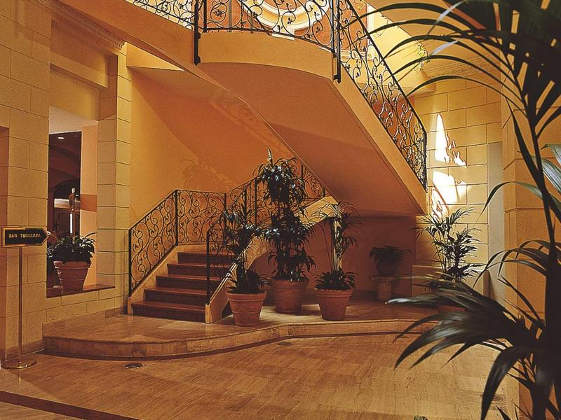 Elegant staircase with curved railing and plants in a warmly lit hotel lobby