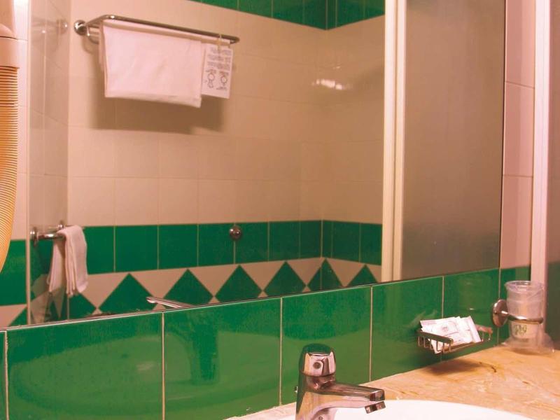 Bright bathroom with green and white tiles, sink, and hanging towel.