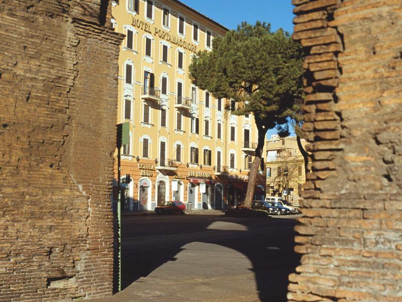 Street scene framed by historic brick walls with a yellow building in the background.