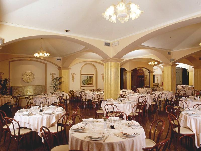 Elegant hotel restaurant with round tables, white tablecloths, and classic wooden chairs.