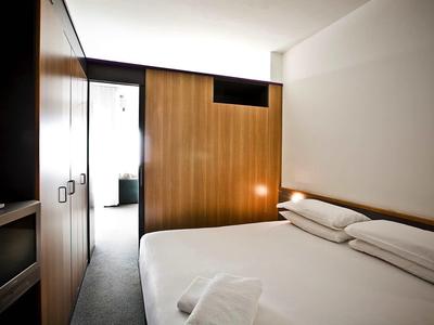 Kompaktes Schlafzimmer mit großem Bett, Holzpaneelen an der Wand und integriertem Licht.