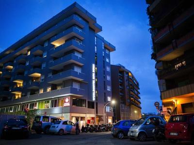 Moderne Wohnhäuser mit Balkonen bei Abenddämmerung, parkende Autos und Straßenbeleuchtung.