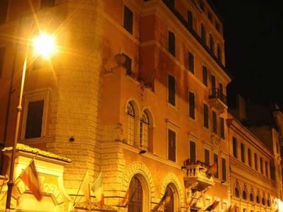 Osvětlená hotelová budova v noci s zaparkovanými auty před vchodem.