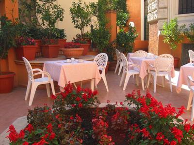 Terrasse mit weißen Plastikstühlen und Tischen mit rosafarbenen Tüchern, umgeben von Pflanzen.