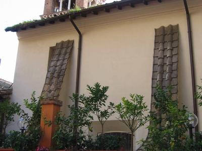 Ein Garten mit Pflanzen in Töpfen vor einem Gebäude, im Hintergrund ein hoher Backsteinturm.