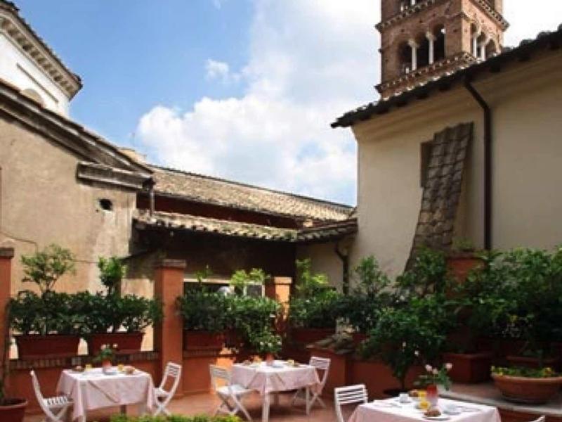 Pohodlná venkovní část hotelu s prostřenými stoly a historickou věží v pozadí.