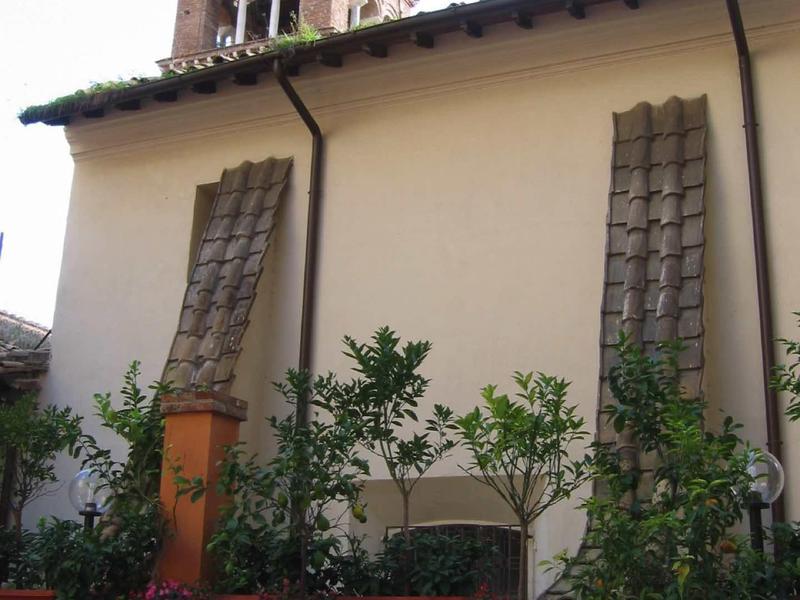 Terasa s stolem a židlemi před budovou s věží v pozadí.