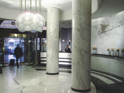 Hell beleuchtete Hotellobby mit Marmorsäulen, modernem Tresen und weichem Lampenschirm.