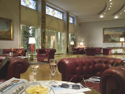 Eleganter Salon mit braunen Ledersofas, großen Fenstern, Gemälden und gedämpftem Licht.