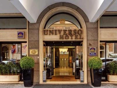 Eingang eines Hotels mit großem Bogen, hölzernen Türen und bepflanzten Töpfen links und rechts.