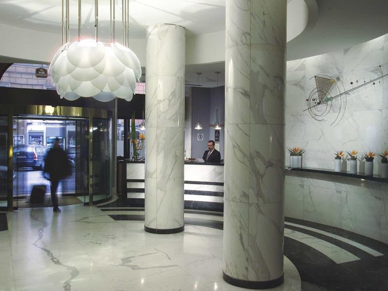 Hell beleuchtete Hotellobby mit Marmorsäulen, modernem Tresen und weichem Lampenschirm.