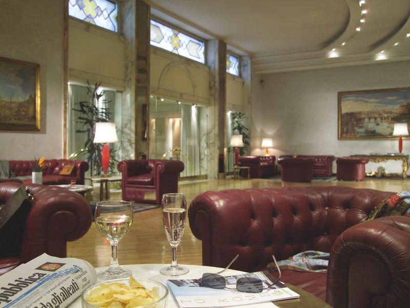 Eleganter Salon mit braunen Ledersofas, großen Fenstern, Gemälden und gedämpftem Licht.