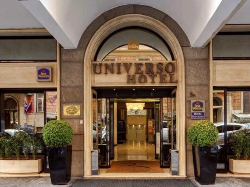 Eingang eines Hotels mit großem Bogen, hölzernen Türen und bepflanzten Töpfen links und rechts.