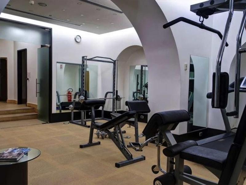 Innenraum eines Fitnessraums mit Trainingsgeräten, Spiegeln und einer Uhr an der Wand.