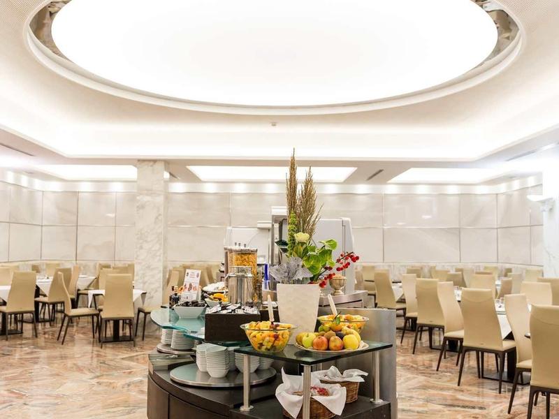 Eleganter Speisesaal mit rundem Buffet, weiß-beigen Stühlen und großem ovalem Deckenlicht.