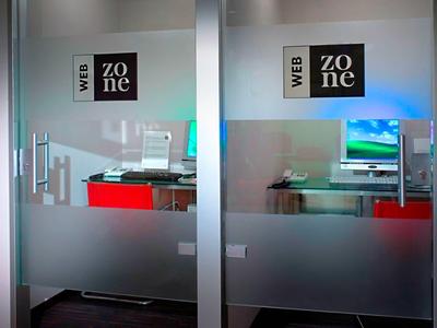 Glaswände mit Aufklebern "WEB zone", dahinter zwei rote Stühle und zwei Computerarbeitsplätze.