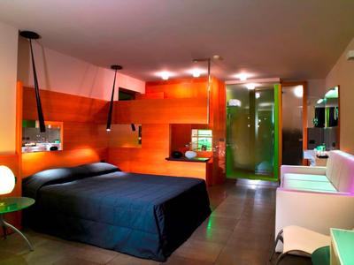 Modernes Schlafzimmer mit dunklem Bett, orangefarbenen Wänden und einer grünen Glastür im Hintergrund.