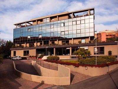 Hotel moderno con grande facciata in vetro e parcheggio su più livelli sotto un cielo nuvoloso.