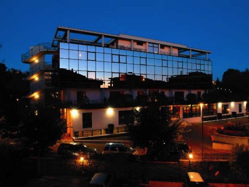 Modernes Gebäude mit großer Glasfassade, beleuchtet in der Abenddämmerung, umgeben von Bäumen.