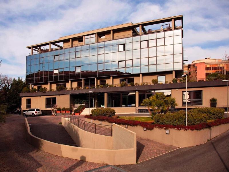 Modernes Bürogebäude mit Glasfassade, eingebettet in Hang, davor kurviger Straßenverlauf und Grünflächen.
