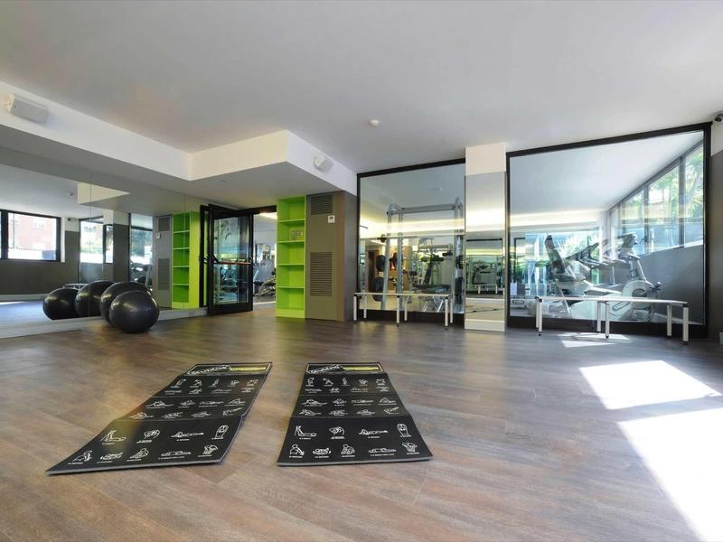 Großer heller Fitnessraum mit Holzfußboden, Spiegeln, Matten und verschiedenen Trainingsgeräten.