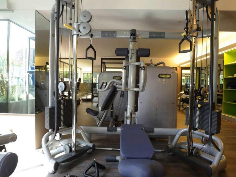 Moderner Fitnessraum mit Krafttrainingsgeräten, blauem Sitz, Holzfußboden und großem Fenster.