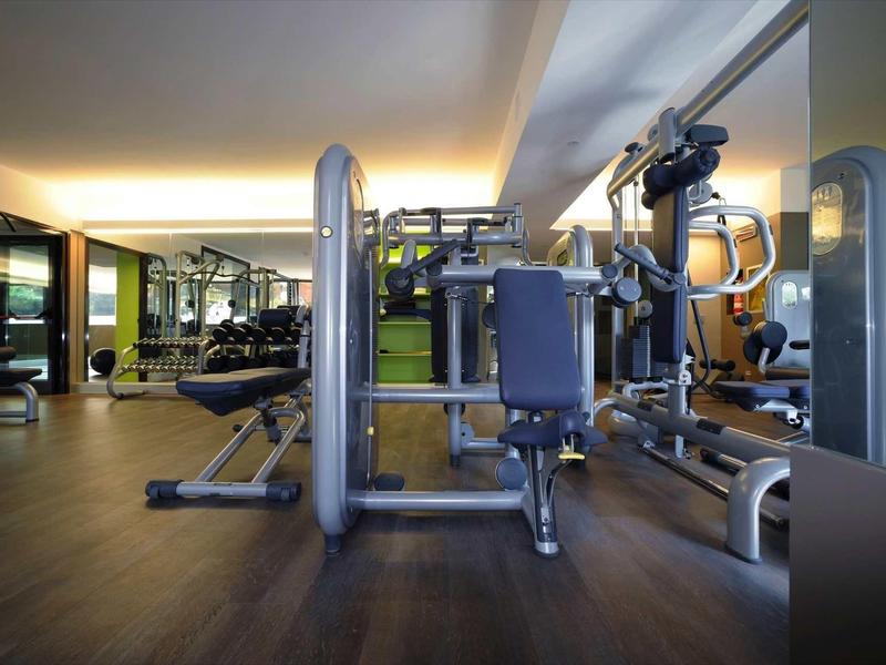 Moderner, gut beleuchteter Fitnessraum mit verschiedenen Geräten auf dunklem Holzboden.