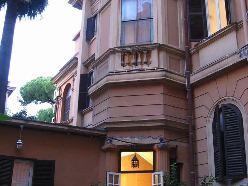 Ingang van een historisch gebouw met open deuren en luiken naast palmbomen.