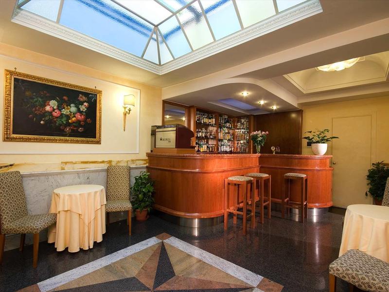 Pohodlný hotelový bar s dřevěným nábytkem, osvětlením a obrazem pod skleněnou střechou.