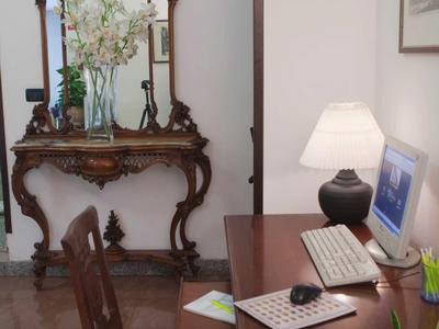 Stůl s počítačem a starožitná zrcadlová konzola s květinami v světlé místnosti.