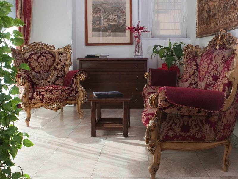 Elegantní posezení s červeným barokním čalouněným nábytkem a dřevěným stolem v světlé místnosti.